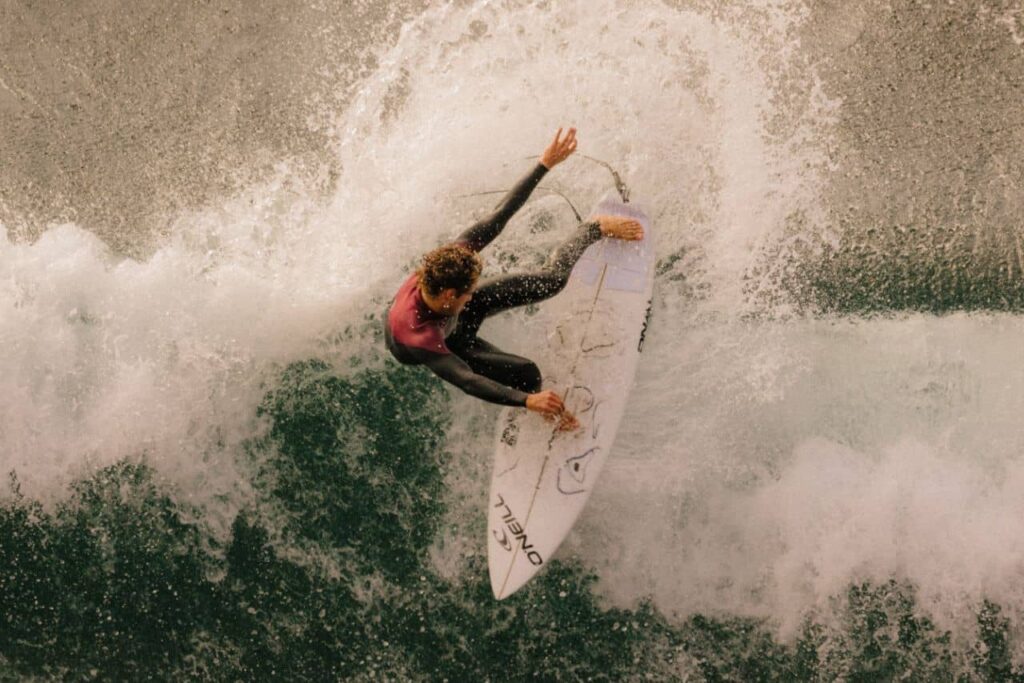 Hombre sobre tabla de surf tomando una ola y haciendo un truco sobre ella.