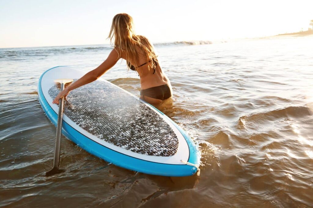 Mujer introduciéndose en el mar junto a una tabla de paddle rígida.