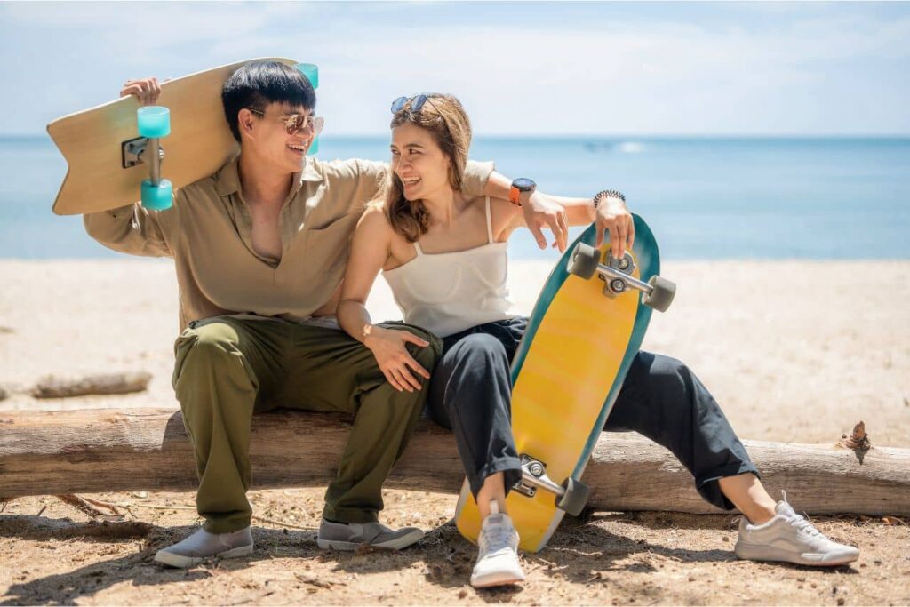 Hombre y mujer sentados en la playa con dos tablas de surfskate.