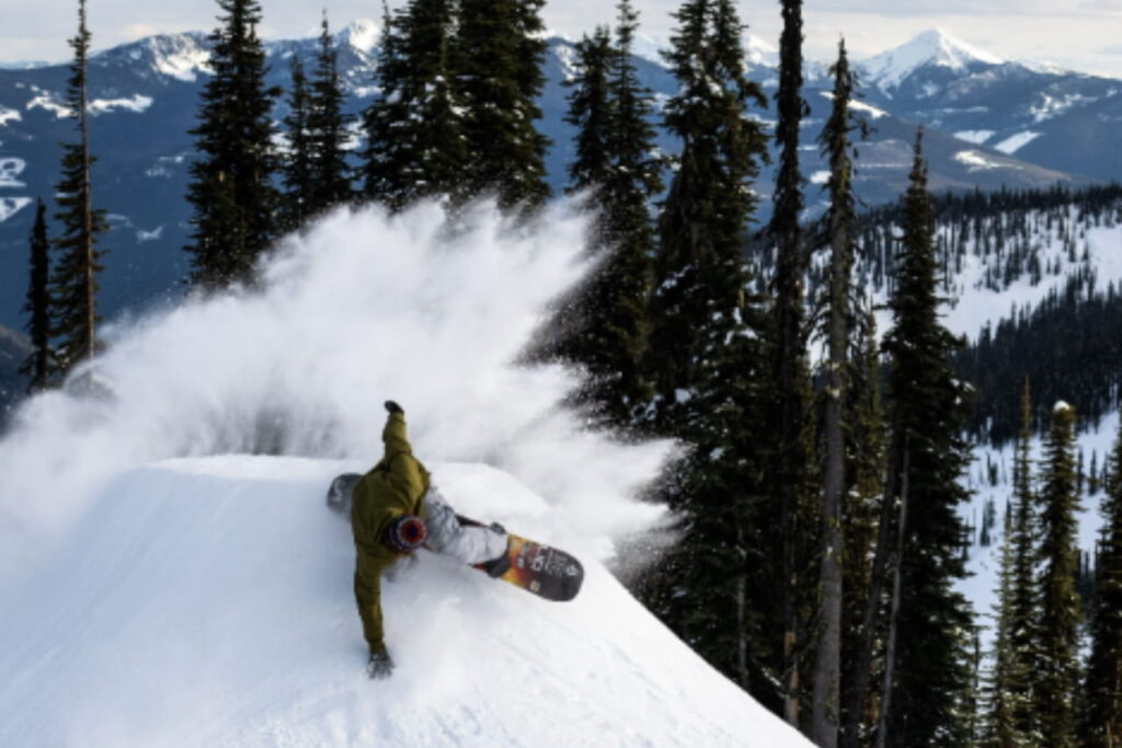 Snowboarder demostrando habilidad junto a su tabla de snow bordeando un montículo de nieve.